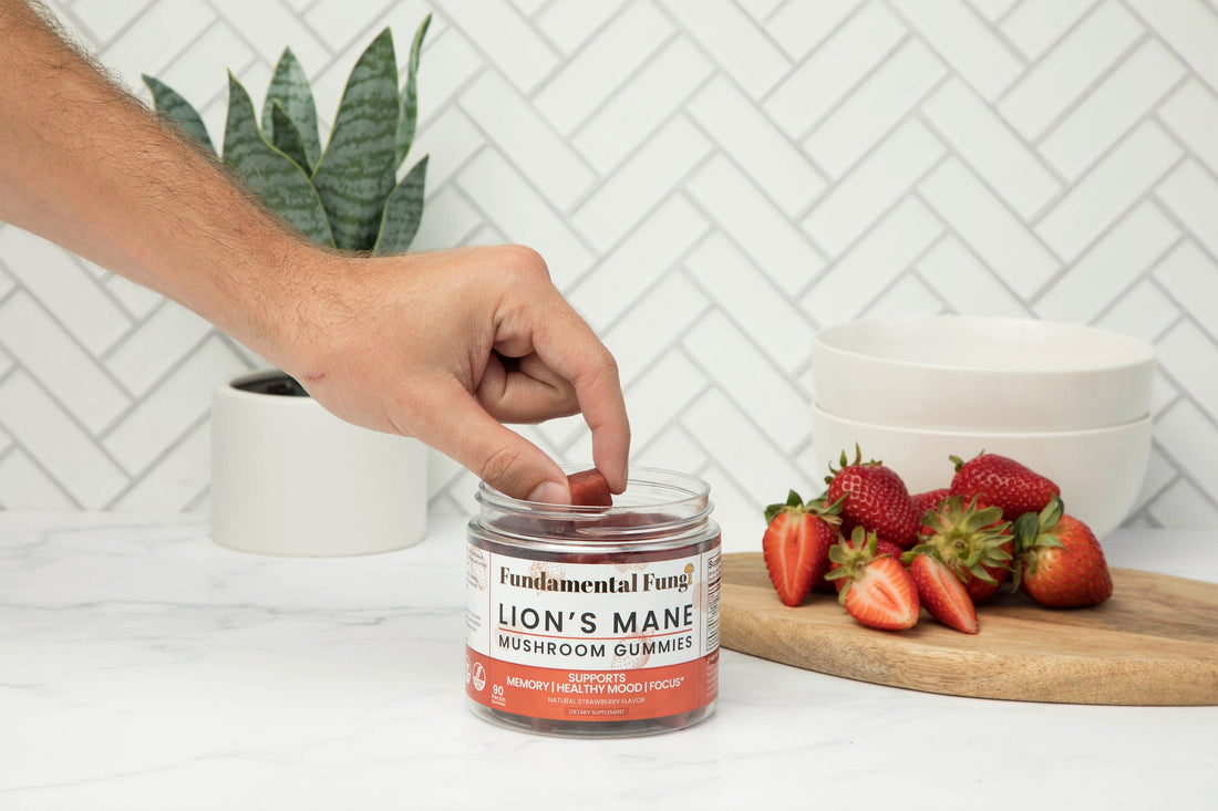 Hand taking a Lion's Mane mushroom gummy from the jar on a kitchen counter with strawberries